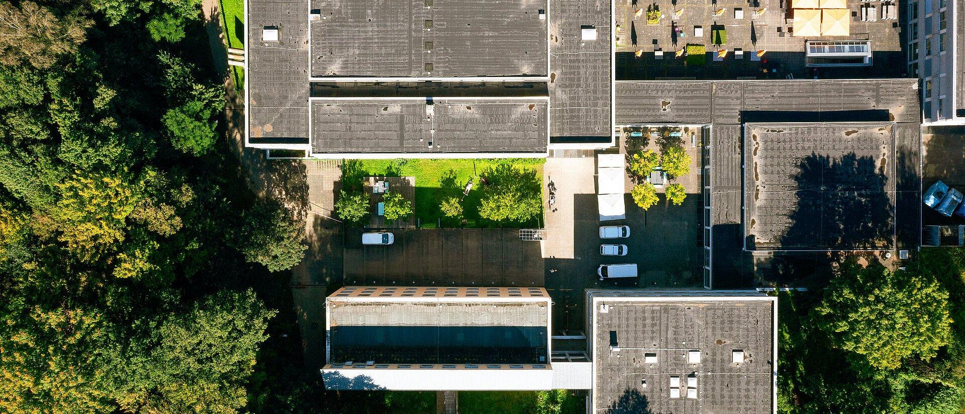 Luftaufnahme: Gebäude mit Flachdächern umgeben von Bäumen.