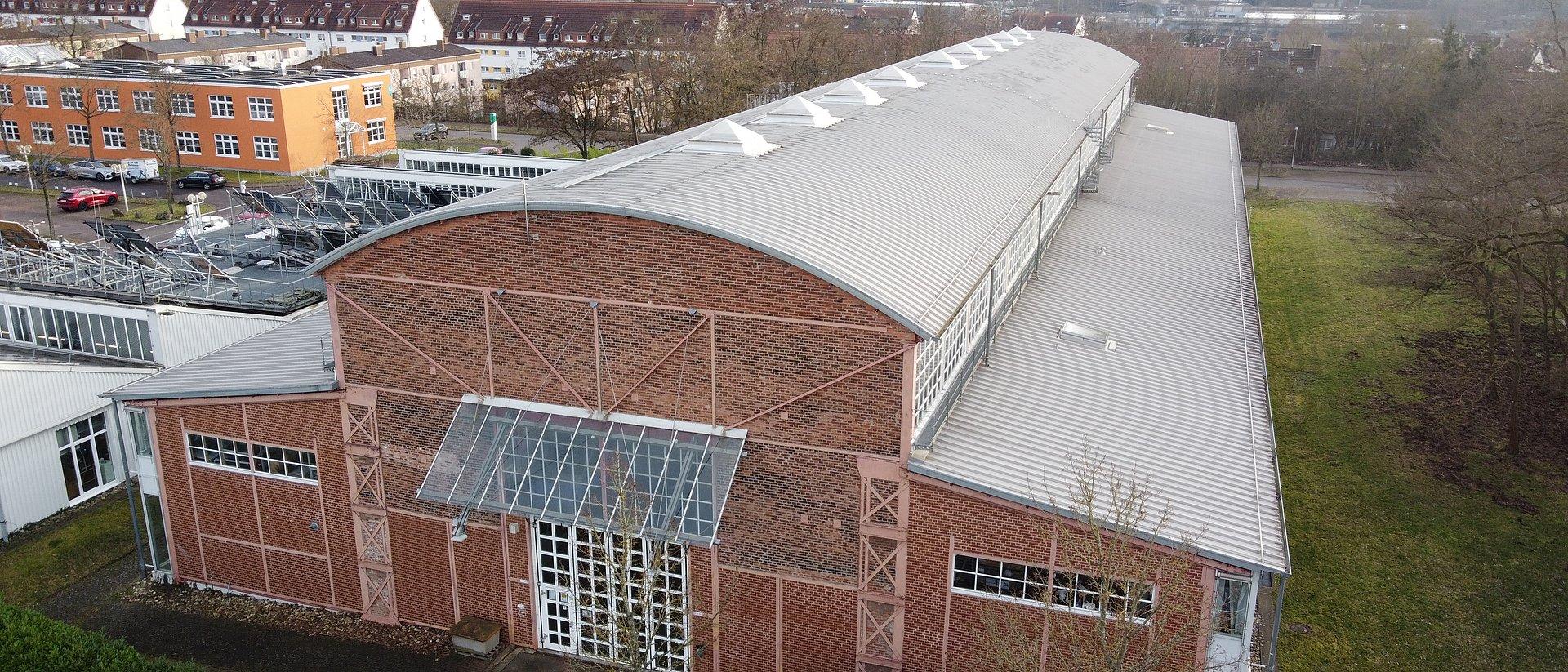 Großes Backsteingebäude mit gewölbtem Dach und Glasfassade, aus der Vogelperspektive.