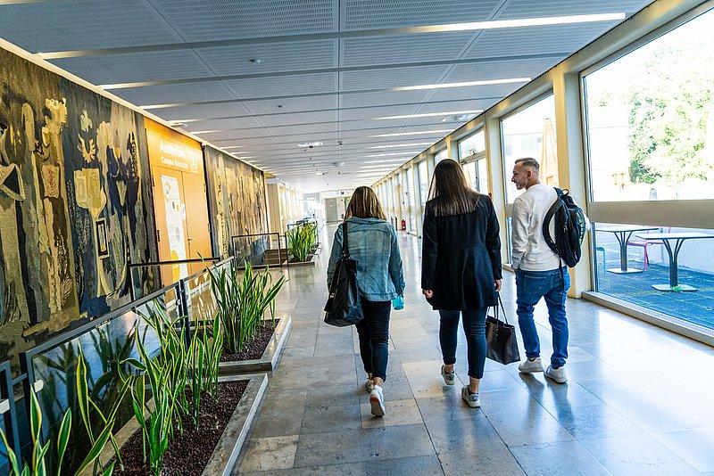 Langer heller Flur mit Wandkunst, Pflanzen und drei Gehenden.