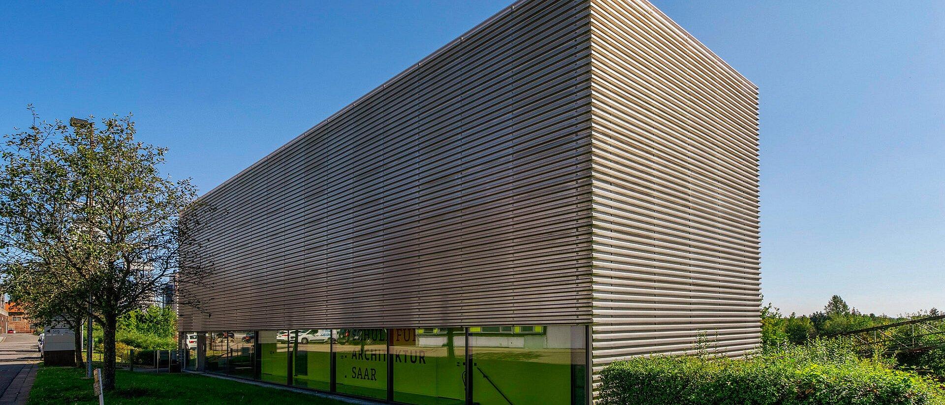 DE: Modernes Gebäude mit Metallfassade und langen Fensterbändern im Erdgeschoss.