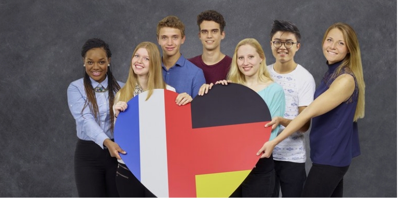 Group of seven people holding a large heart with country flags.