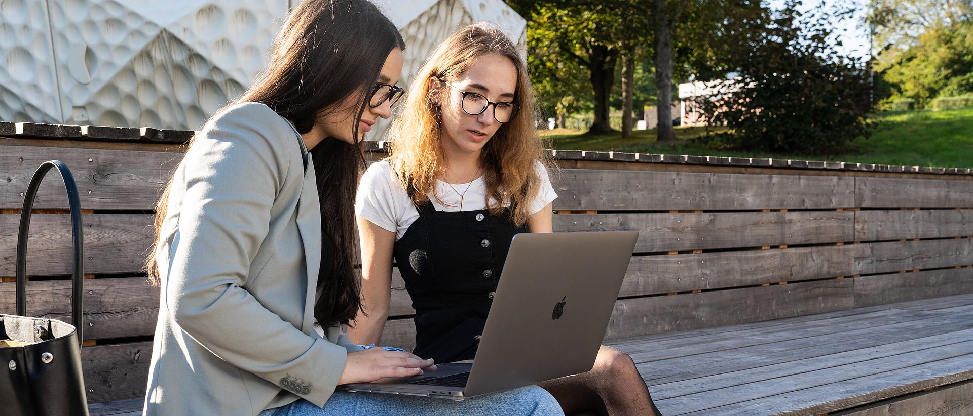 Zwei Personen sitzen draußen und arbeiten am Laptop.