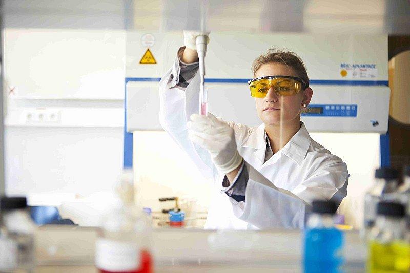 Person im Laborkittel pipettiert Flüssigkeit in einem Labor.